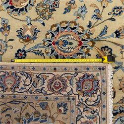 Persian Kashan carpet, beige ground, field with an all-over design of scrolling palmettes and floral sprays in blue and terracotta within a ivory ground and pale blue floral border
