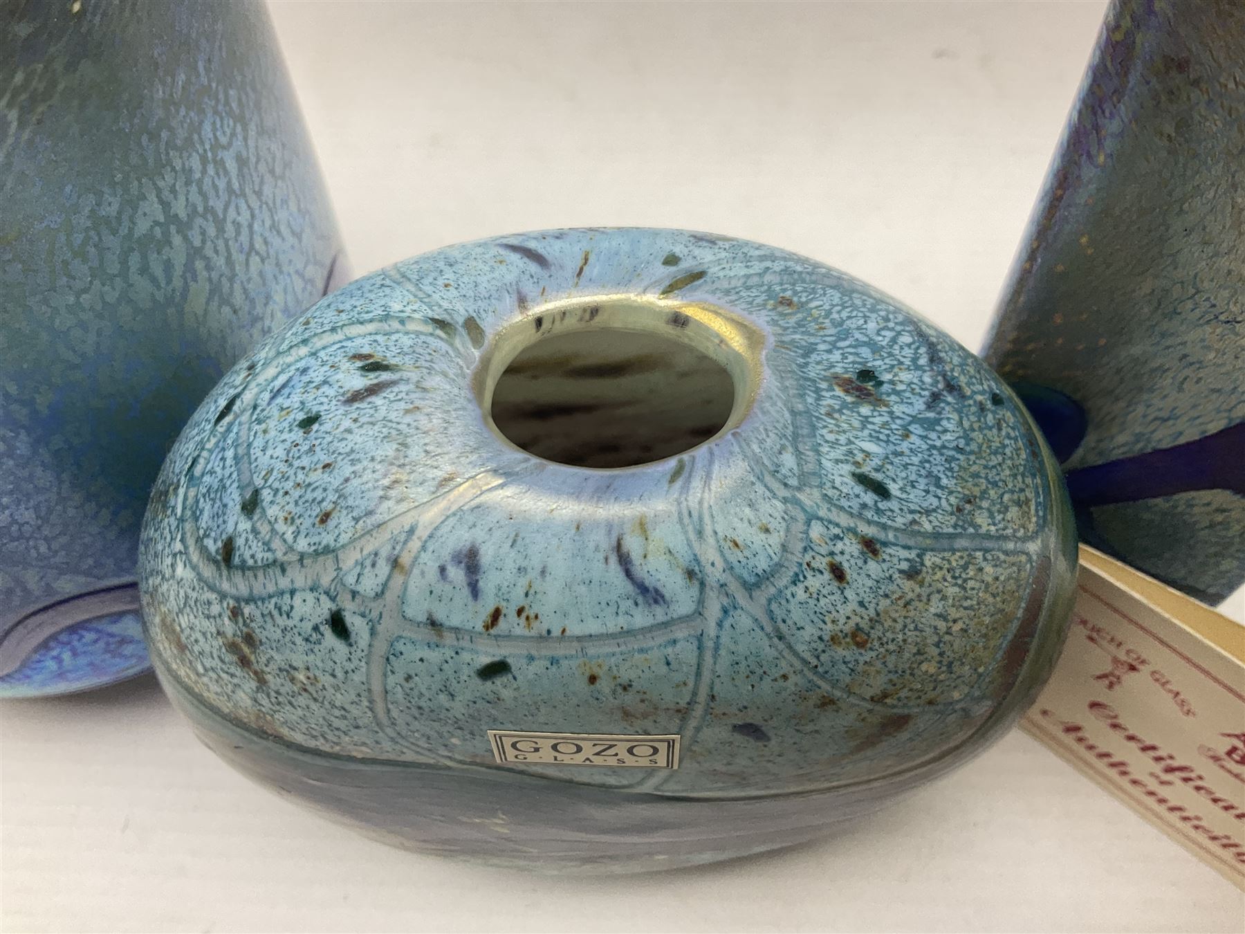 Two Isle of White glass vases, by Alum Bay Glass, both with blue swirl design upon an iridescent mottled blue/green ground, together with a Gozo Glass vase of pebble form, with similar design, H12cm