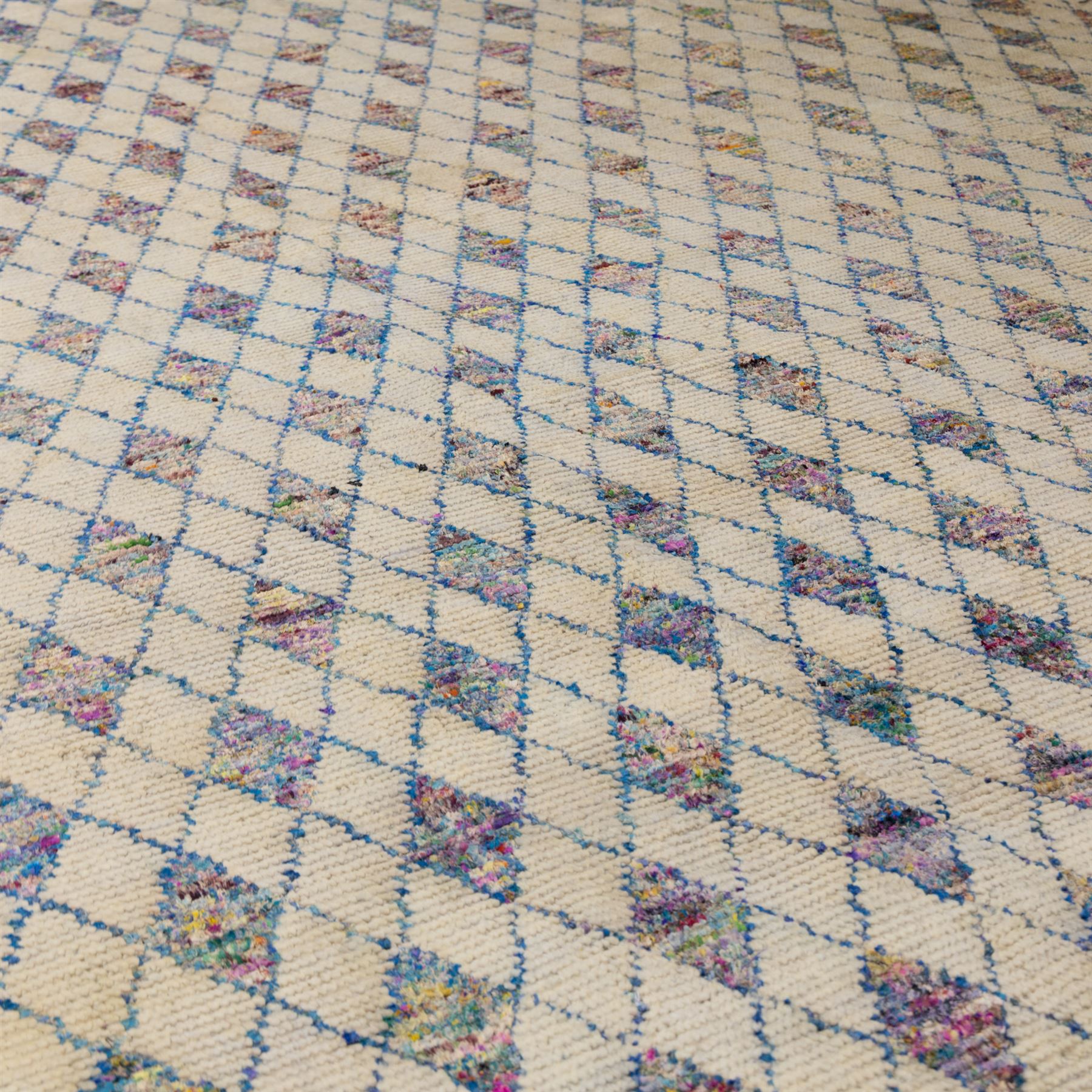Contemporary Moroccan Berber design wool rug, cream field with blue diamond lattice, decorated with repeating multicoloured lozenge motifs, short fringe ends and bound sides