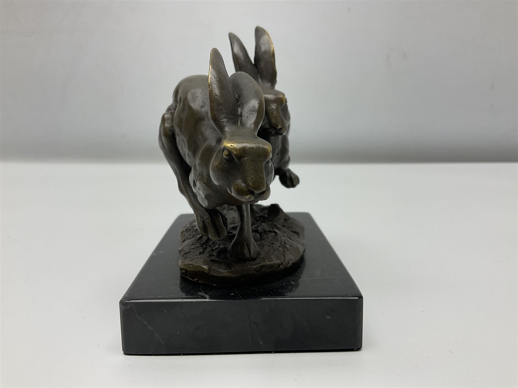 Bronze figure group, modelled as two hares in chase, upon a naturalistic base signed Nick and with foundry mark, raised upon a rectangular marble base, overall H12cm. 