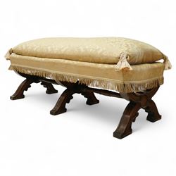 Late Victorian Gothic revival walnut long stool, rectangular padded seat upholstered in cream damask with tasselled corners and fringe border, raised on twin X-frame supports united by a turned stretcher, circa 1880