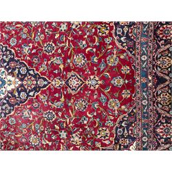 Pair of Persian wool rugs, each with rich red ground, one centred with a diamond-shaped medallion and navy spandrels within a floral field, the other with radiating floral medallion and scrolling foliate motifs, both enclosed by multiple borders with palmette and flowerhead designs, from the region of Kashan 291x376, 299 x 378 