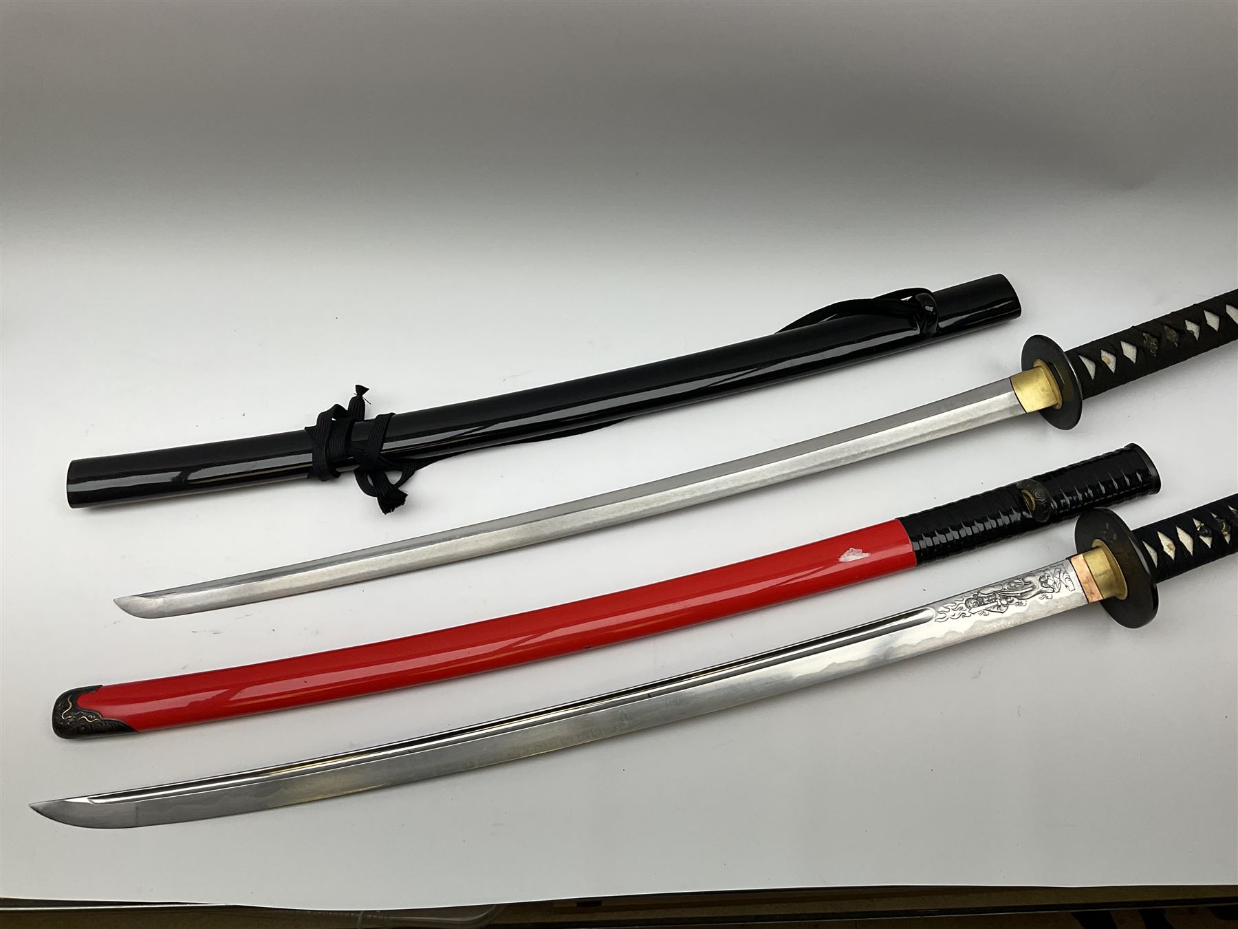 Reproduction Japanese sword daisho of katana and wakisashi with matching tanto; together with another reproduction katana; all with simulated fish skin grip and lacquered saya (4)