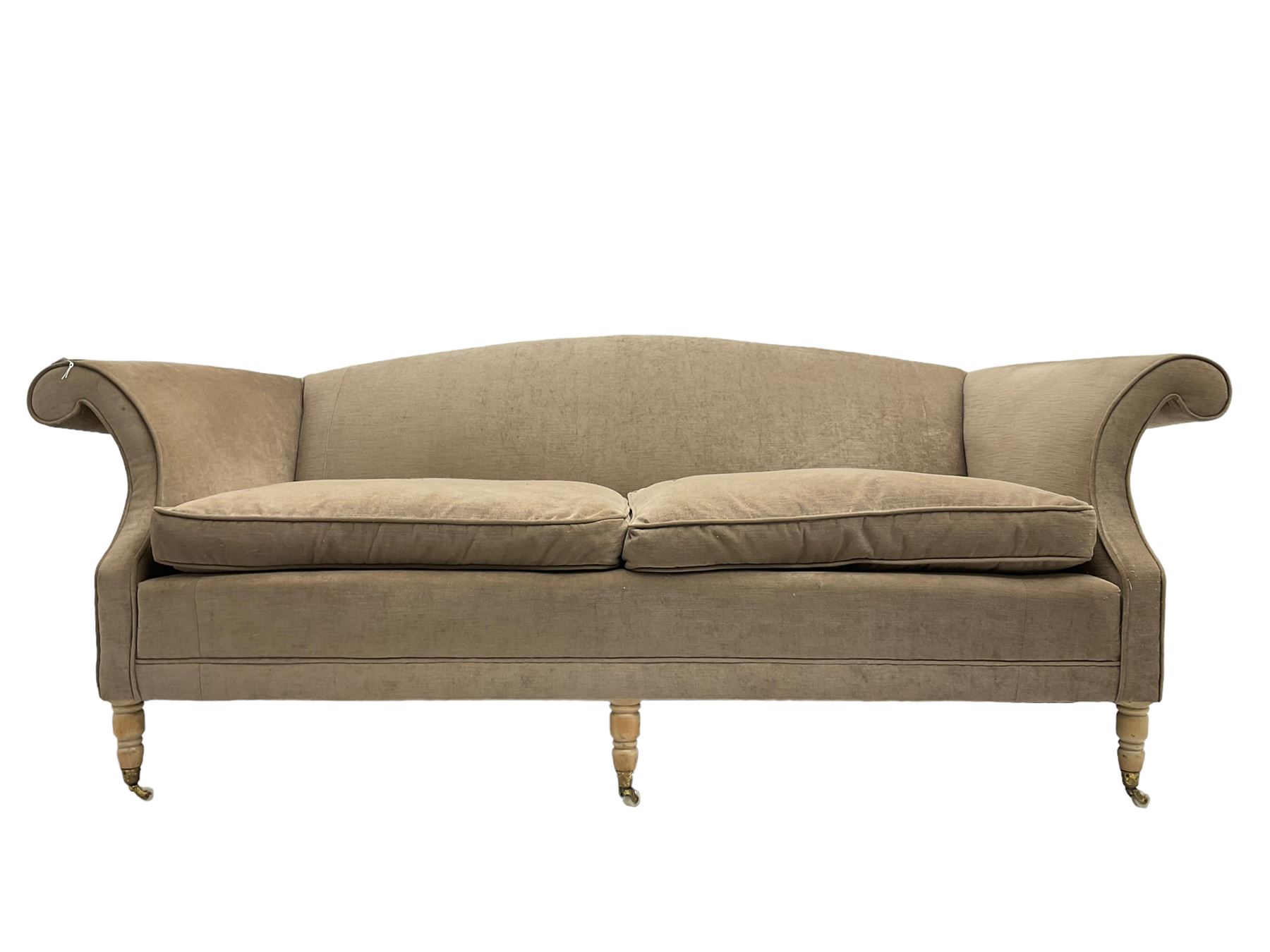 Traditional three seat sofa, curved back over scrolled arms, upholstered in crushed beige fabric with matching loose cushions, on turned front supports with brass and ceramic castors, together with matching footstool