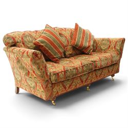 Duresta - traditional shape two-seat sofa with out-swept arms, upholstered in crimson ground fabric decorated with palmettes and foliate motifs with matching loose and scatter cushions, raised on compressed bun feet with brass cups and castors