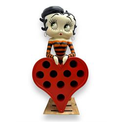 Contemporary large-scale Betty Boop painted wine rack, modelled leaning against a heart-shaped stand with ten circular bottle slots, dressed in black and orange striped attire