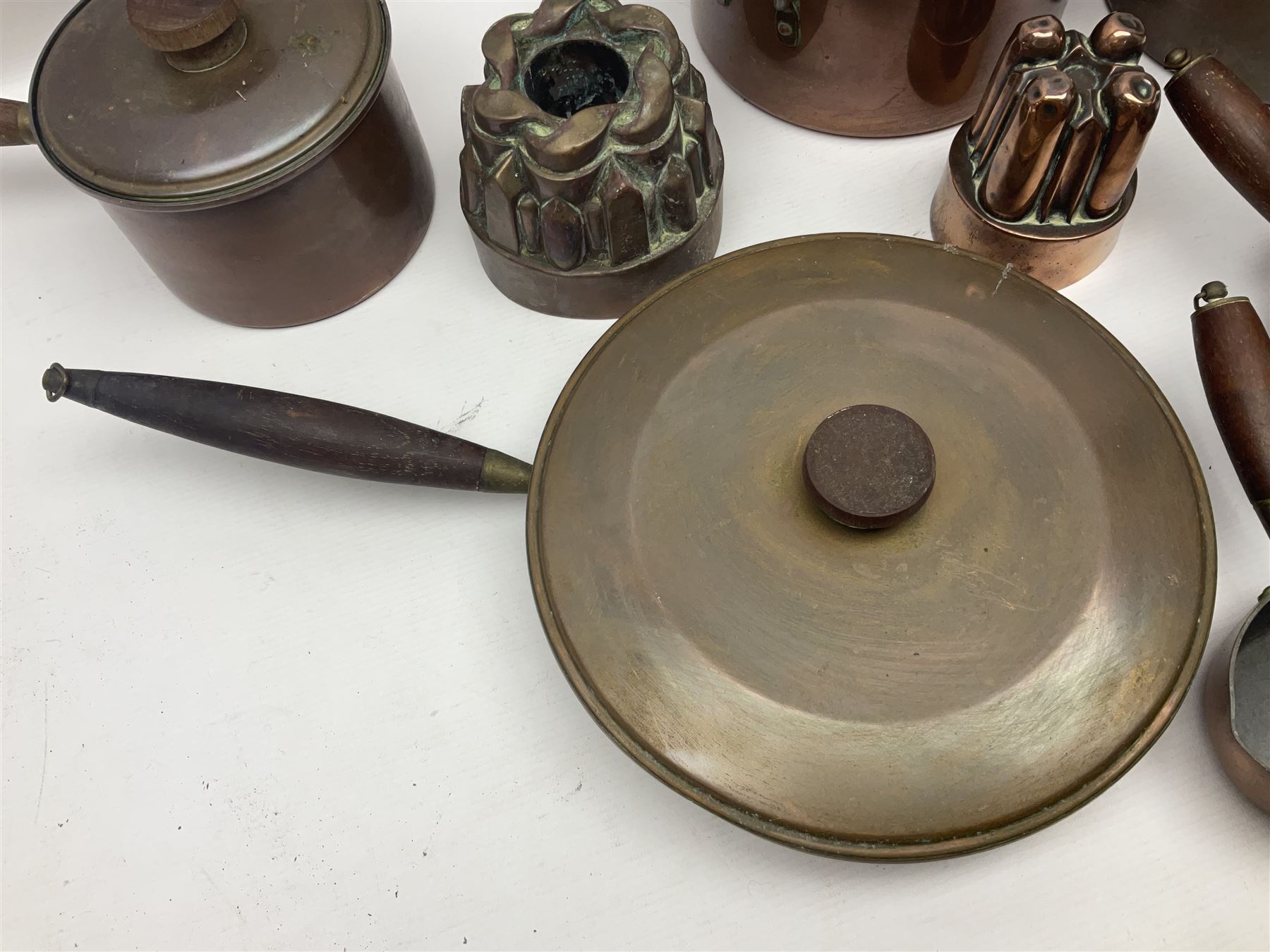Four Victorian copper moulds, together with a graduating set of copper pans with wooden handles and finials to covers, largest pan 