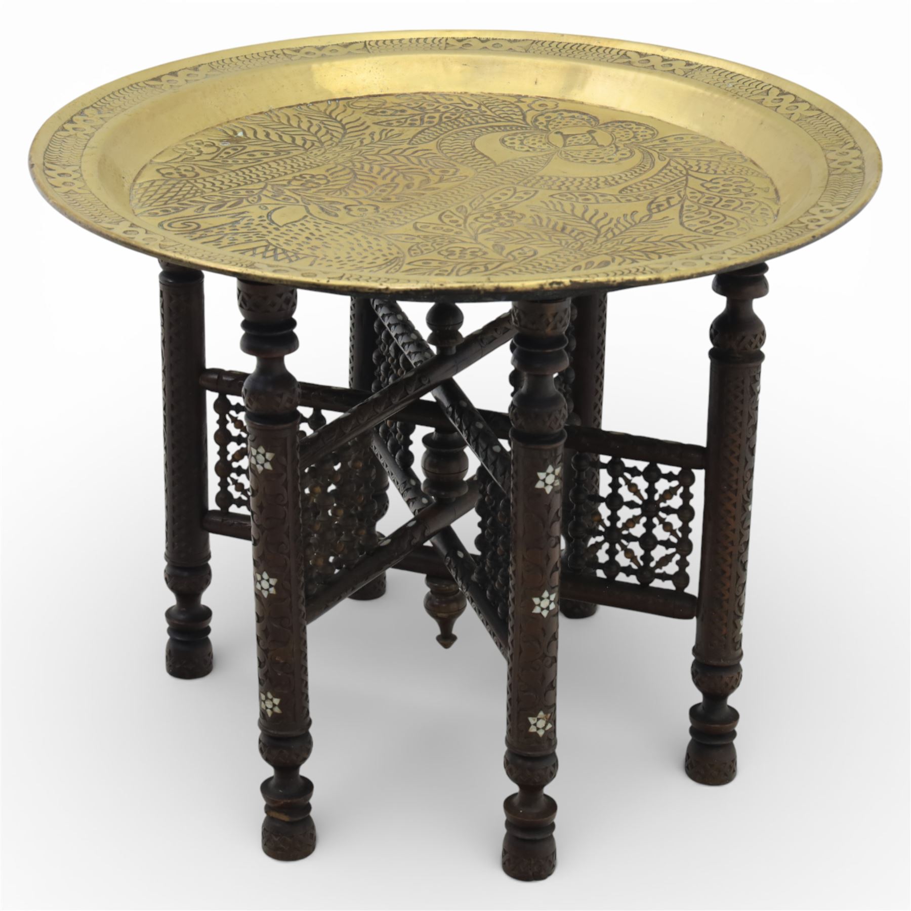 20th century Eastern brass charger topped table, the circular brass trap chased with an elephant, palm tress and flowering vines, supported upon a folding stand with six turned legs with inlaid detail, united by turned supports