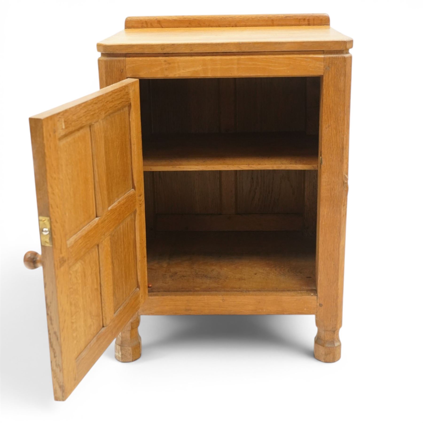 Mouseman - adzed and panelled oak bedside cupboard of small proportions, raised back over rectangular canted top, fitted with single panelled cupboard door with chamfered rails and turned knob handle, enclosing single shelf, raised on octagonal feet,  carved with mouse signature, by the workshop of Robert Thompson of Kilburn