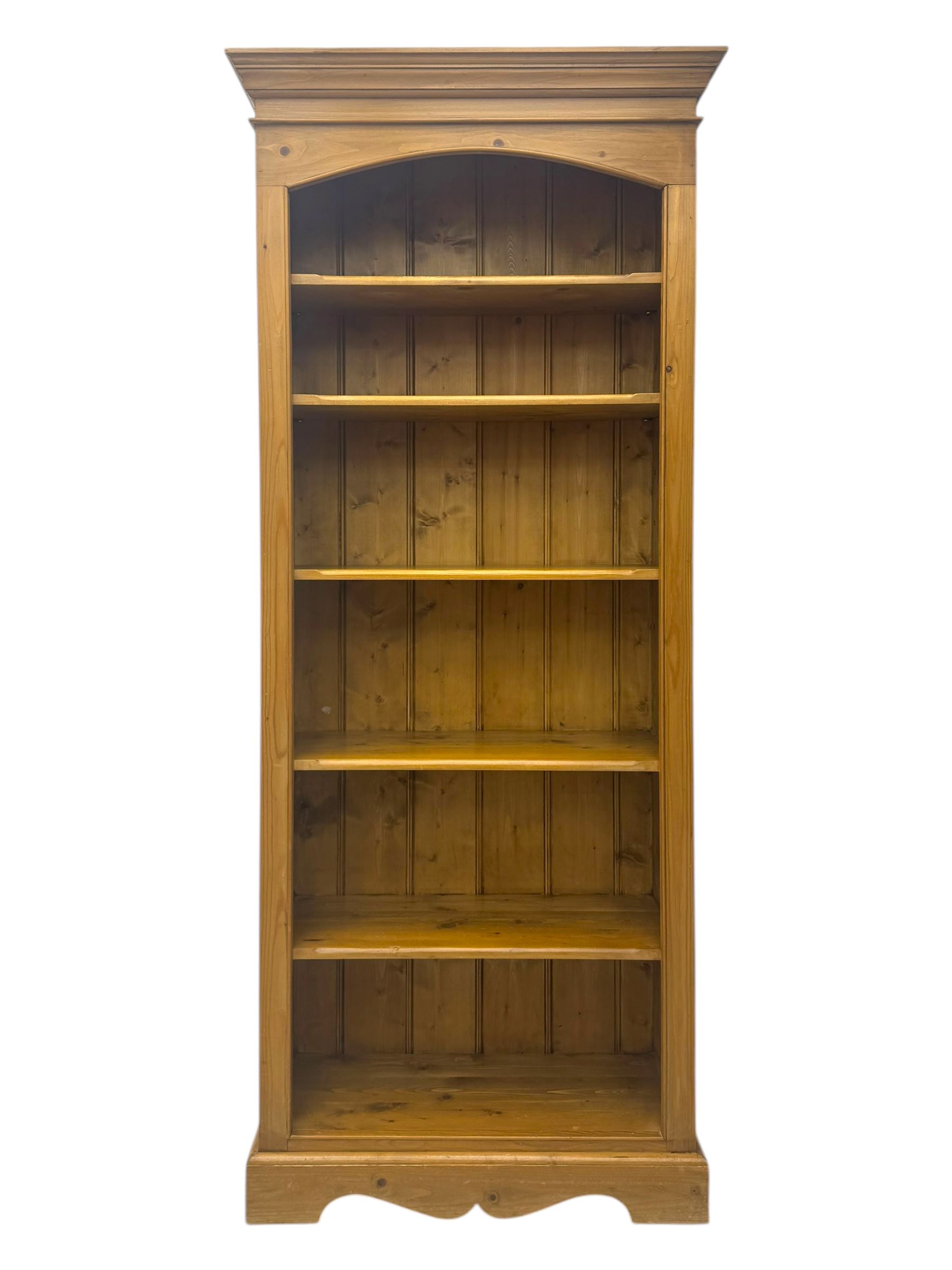 Early 20th century pine bookcase, projecting cornice over arched open shelving area with five adjustable shelves, on shaped plinth base