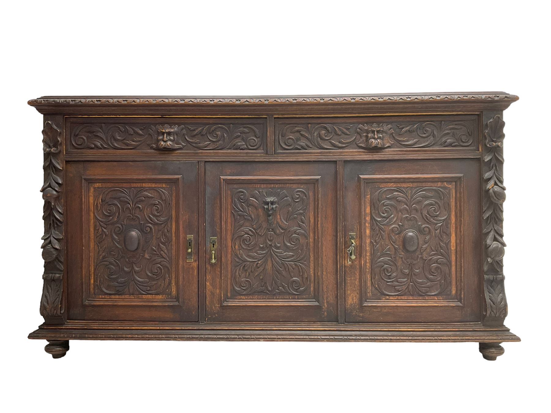 Victorian heavily carved oak sideboard, the moulded top carved with foliate decoration to the edge, fitted with two drawers and three cupboards, the drawer fronts carved with green man mask handles and scrolling foliage, the panelled doors carved with interlacing foliage, on turned compressed bun feet