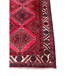 Persian Hamadan red ground rug, decorated with six stepped lozenge medallions, the guarded border with repeating stylised flower head decoration, with inscription to corner