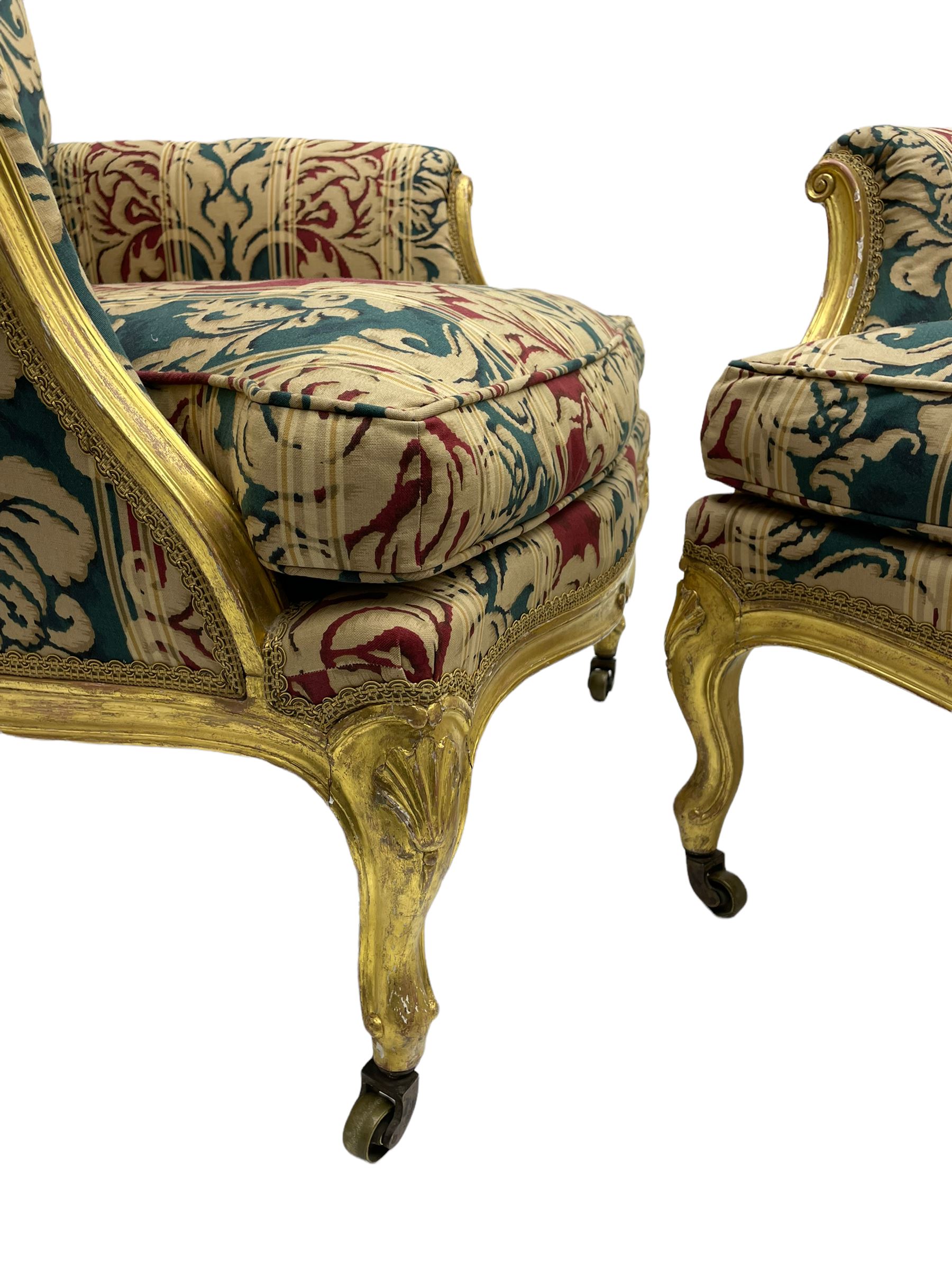 William Bertram & Son of London - pair late 19th century giltwood armchairs, moulded frame with scroll carved back and arm terminals, upholstered in striped fabric with foliate pattern, on shell carved cabriole supports, the brass castors stamped 