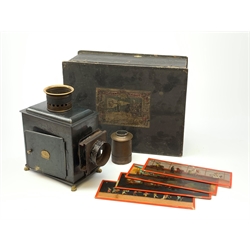 Ernst Plank magic lantern with black japanned body, brass chimney and lion paw feet, in original ebonised box with seven 24cm coloured glass slides including Transport Through the Ages etc, the hinged lid with paper labels to both sides W36cm