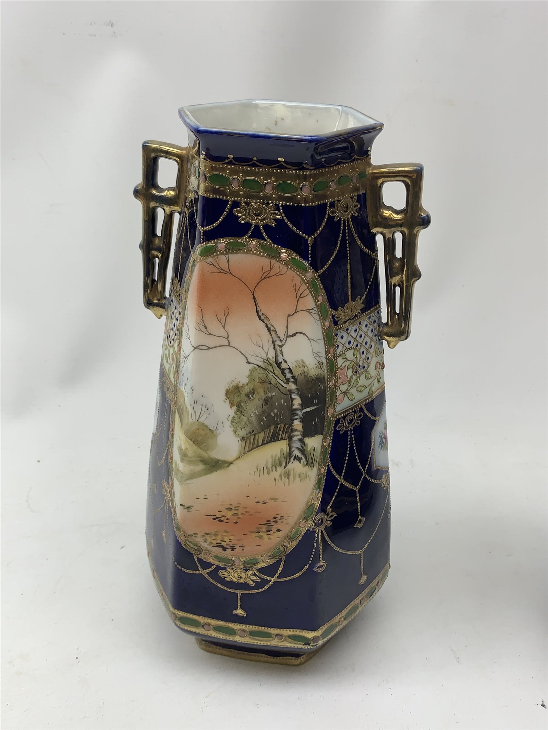 A pair of Japanese Nippon Kinjo vases, of tapering hexagonal form with twin stylised handles, the cobalt blue ground with oval hand painted panels to front and verso depicting landscapes, further detailed with smaller floral bands and panels and heightened with gilt, each with mark beneath, H30.5cm.  
