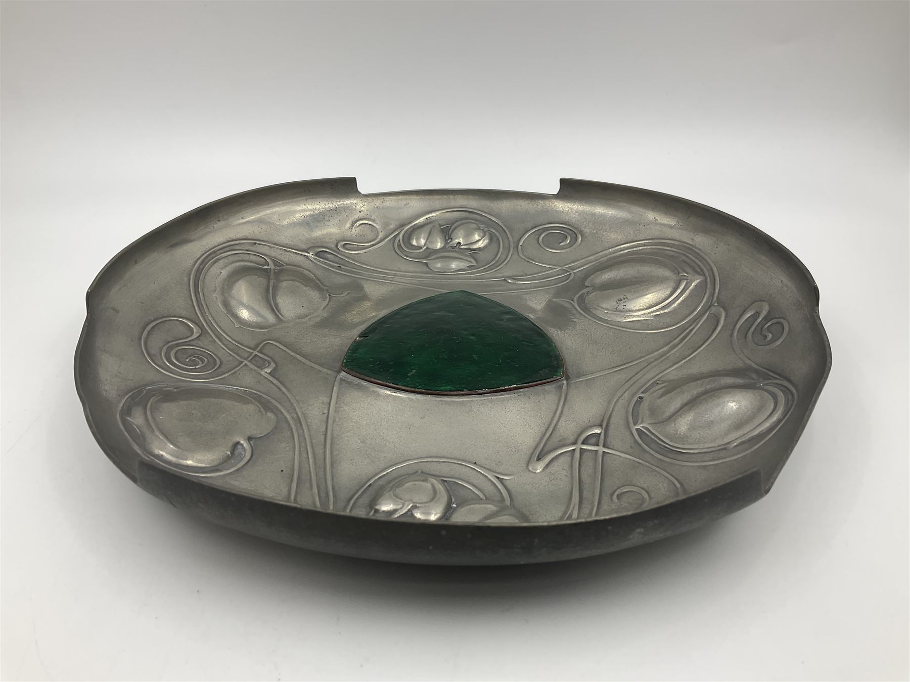 Liberty & Co Tudric pewter Bollelin tray, designed by Archibald Knox, of circular form with shaped edge, cast in relief with foliate tendrils surrounding a green enamel cartouche, impressed beneath Made by Library & Co English Pewter 044, D25.5cm