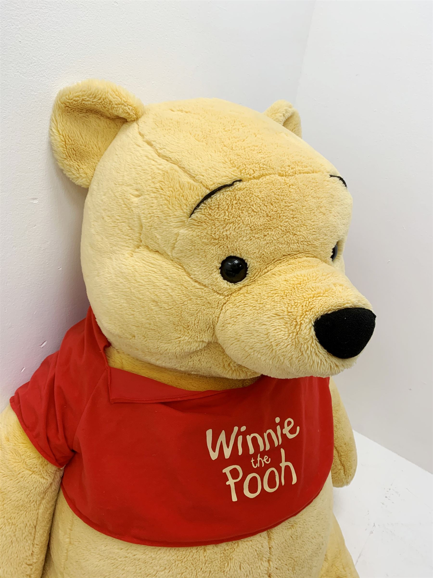 Very large plush covered figure of Winnie The Pooh in a seated position with black plastic eyes, black felt nose and eyebrows, red open mouth and T-shirt with name to front H42