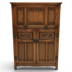 Old Charm - carved oak bar with three bar stools and associated Old Charm drinks cabinet, carved top with channels for glassware beneath, bar surface above glazed panels, shelves for glassware to the back, associated Old Charm drinks cabinet with fall front linenfold carving, above twin doors with shelved interior