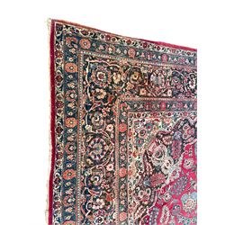 Large Persian red ground carpet, the field decorated profusely with stylised plant and trailing leaf branches, central medallion with projecting floral decoration, the spandrels decorated with further floral motifs, guarded border with repeating floral and scrolling branch pattern 