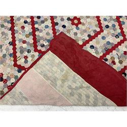 19th century patchwork quilt, hand stitched from hexagons of various materials including printed patterned and floral examples, featuring repeating large central hexagon to centre, the top and bottom with thick panel red jacquard border, the sides bordered with plain red fabric, lined with panels to reverse, 180 x 190 cm