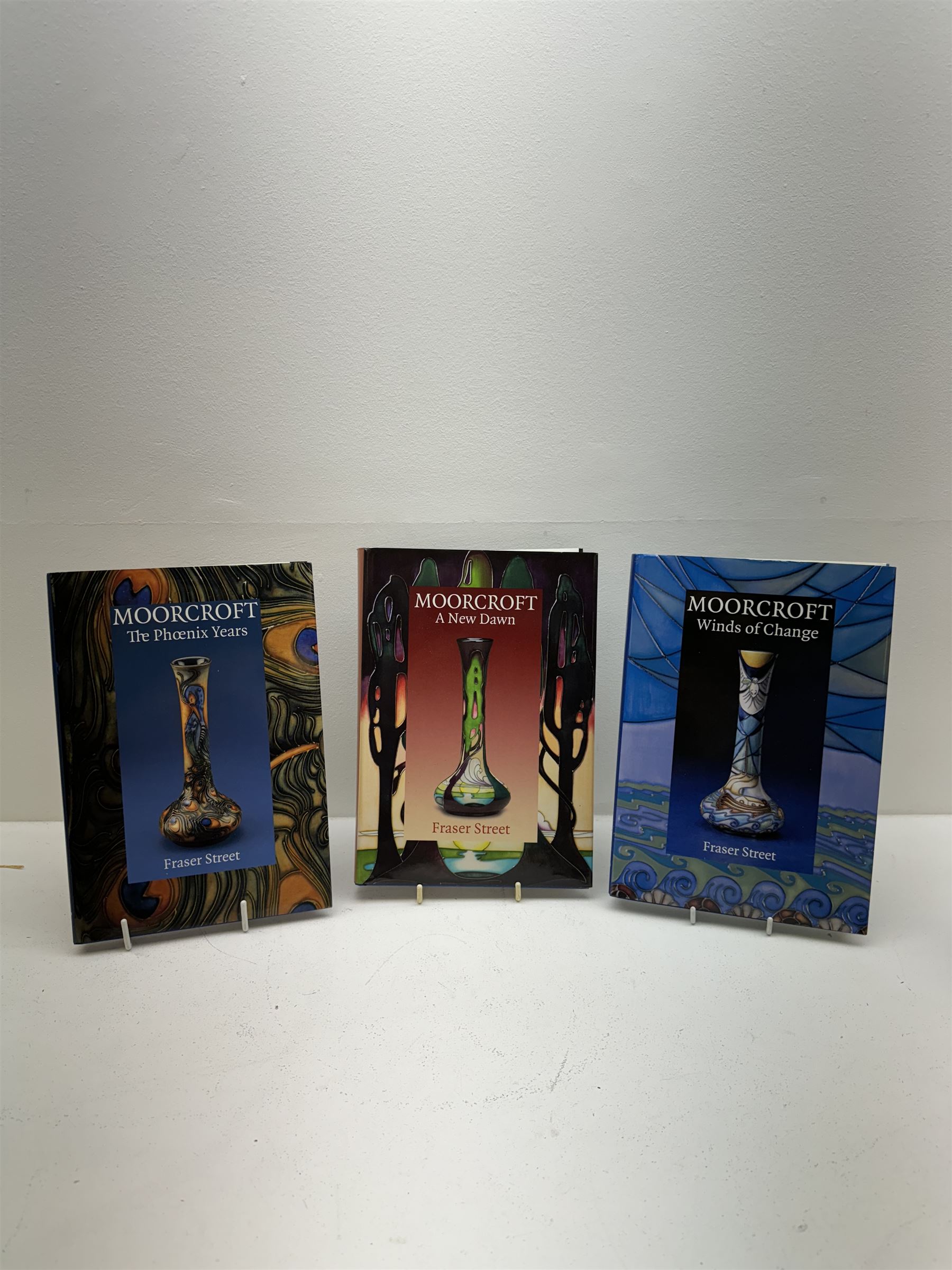 Three Moorcroft reference books, comprising Winds of Change, The Phoenix Years and A New Dawn, together with a collection of Moorcroft magazines 