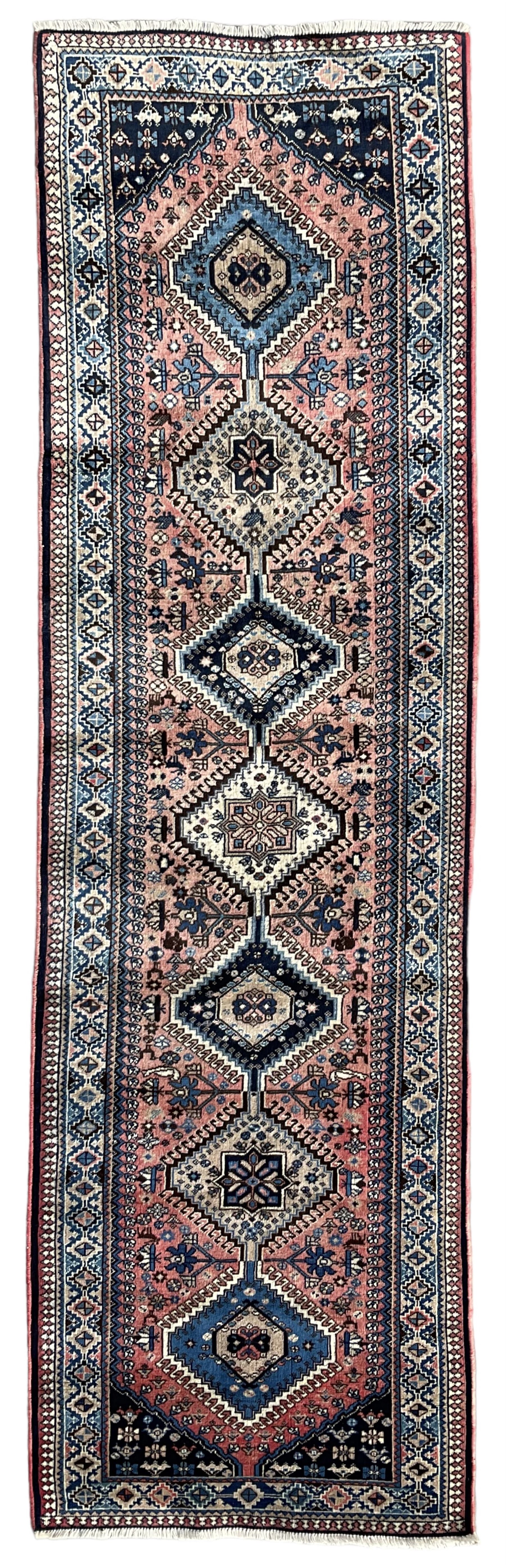 Persian Yalameh coral ground runner rug, the field decorated with seven hooked lozenge medallions surrounded by stylised plant motifs, the indigo spandrels decorated with similar patterns, guarded border with repeating diamond lozenges