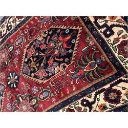 Persian Hamadan rug, the red ground field decorated with two floral medallions and stylised flower heads, repeating guarded border