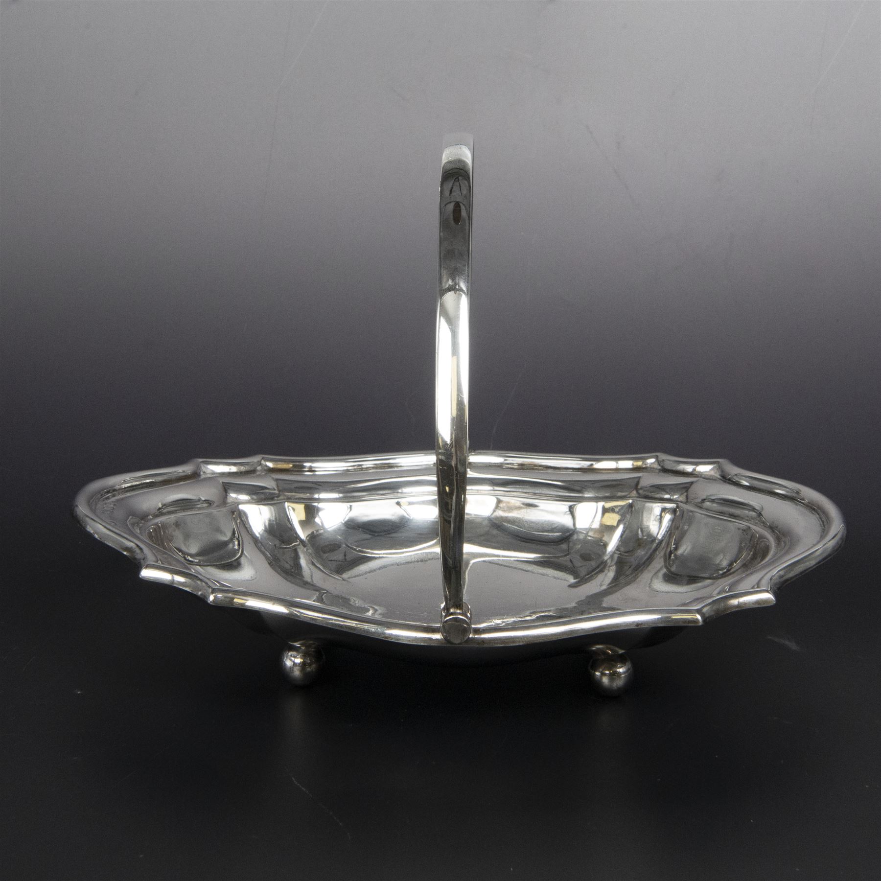 Early 20th century silver swing handled basket, of oval form with shaped rim and upon four bun feet, hallmarked C W Fletcher & Son Ltd, London 1918