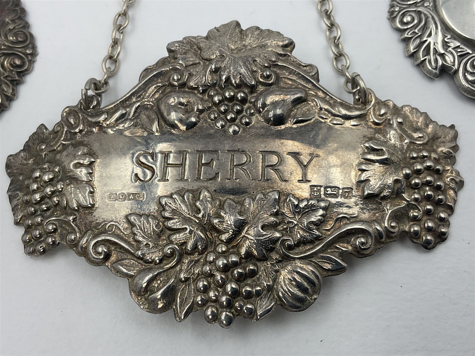 Five modern silver decanter labels, to include three similar Sherry and Brandy examples embossed with scrolls, two hallmarked C Robathan & Son, Birmingham 1989, and one hallmarked Laurence R Watson & Co, Birmingham 1987, together with a scotch example, hallmarked A Marston & Co, Birmingham 1970, and a larger sherry example, embossed with fruiting vines, hallmarked A Marston & Co, Birmingham 1993