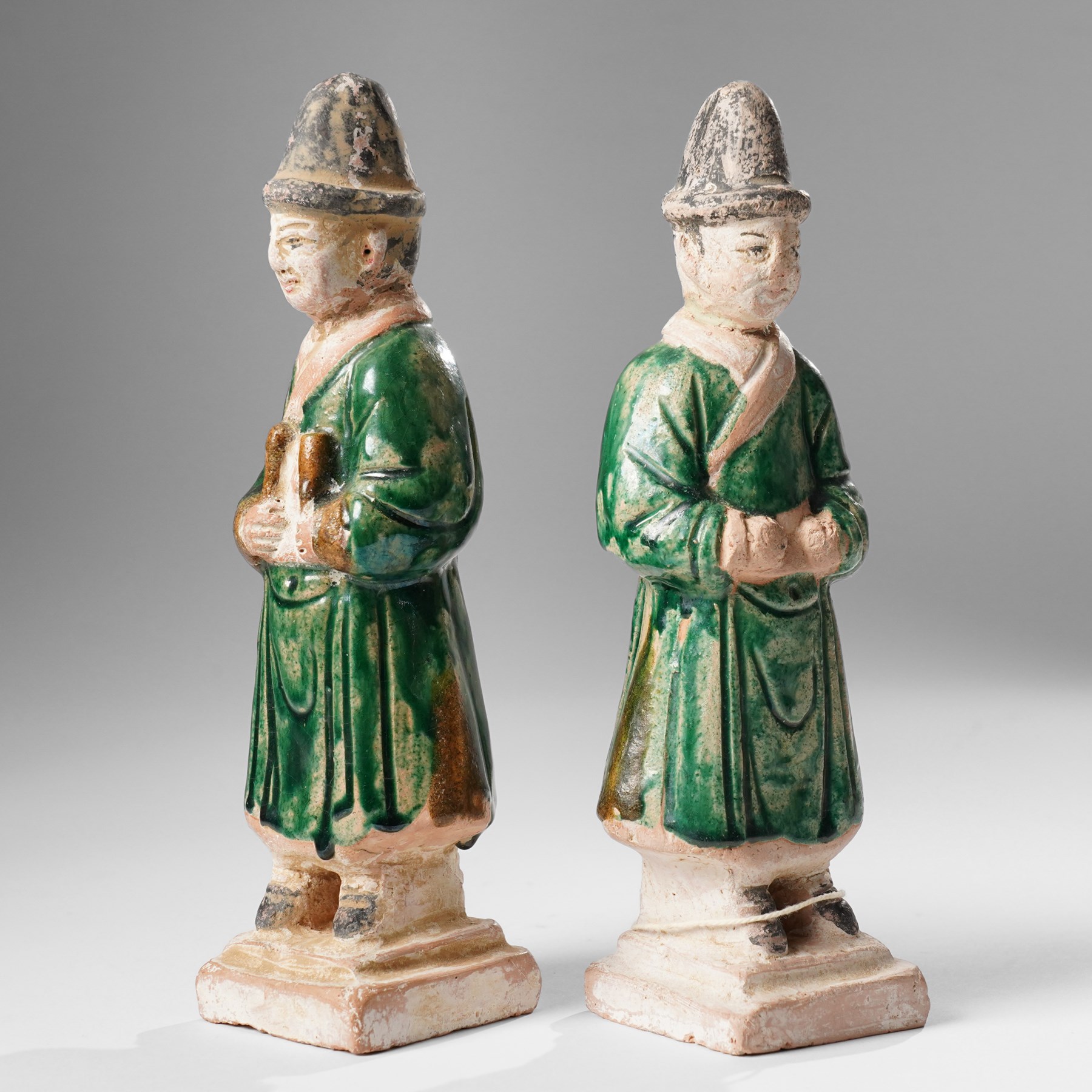Pair of Chinese terracotta court attendant tomb figures,  probably Ming Dynasty, in Sancai green glaze, upon stepped square bases, H22cm 