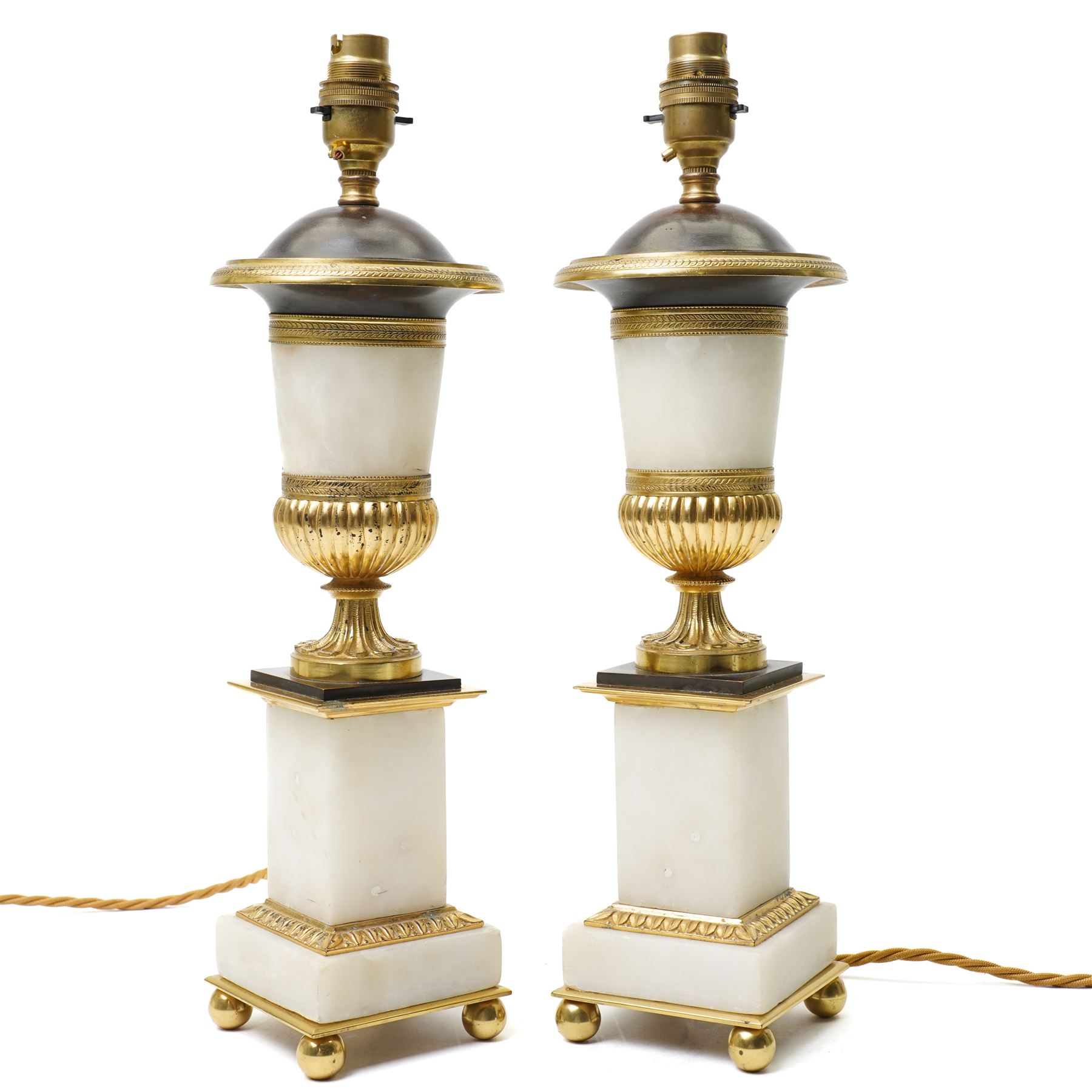 Pair of early 20th-century Neoclassical lamp bases in gilt bronze and alabaster, each decorated with classical figural reliefs celebrating the arts, each of baluster form, the alabaster bodies applied with finely cast gilt-bronze scenes including a seated painter at an easel, a sculptor at work, and allegorical female figures with musical  and theatrical motifs, mounted on square alabaster plinths with gilt-bronze borders and raised on bun feet, the domed shoulders enriched with laurel-leaf mouldings, H42cm 
