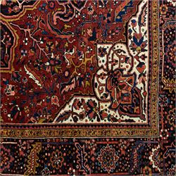 North West Persian Ahar hand-knotted carpet, madder red ground, with a large central shaped floral medallion with pendants, surrounded by angular scrolling foliate motifs incorporating rosettes, palmettes and stylised flowerheads, enclosed by ivory spandrels and a dark navy border with repeating floral motifs and meandering vines, flanked by narrow floral guard stripes, with cotton fringes