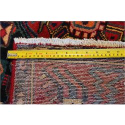 North West Persian Heriz hand-knotted rug, madder red field with an all-over lattice of stepped lozenge medallions enclosing stylized geometric floral motifs and ivory reserve panels, framed by angular vinery and motif borders, main border with with stylized rosettes and geometric devices, flanked by narrow guard stripes,, cotton fringe ends 