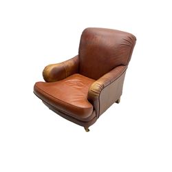 Traditional shaped armchair, scrolled back, upholstered in tan leather, raised on turned supports with brass cups and castors