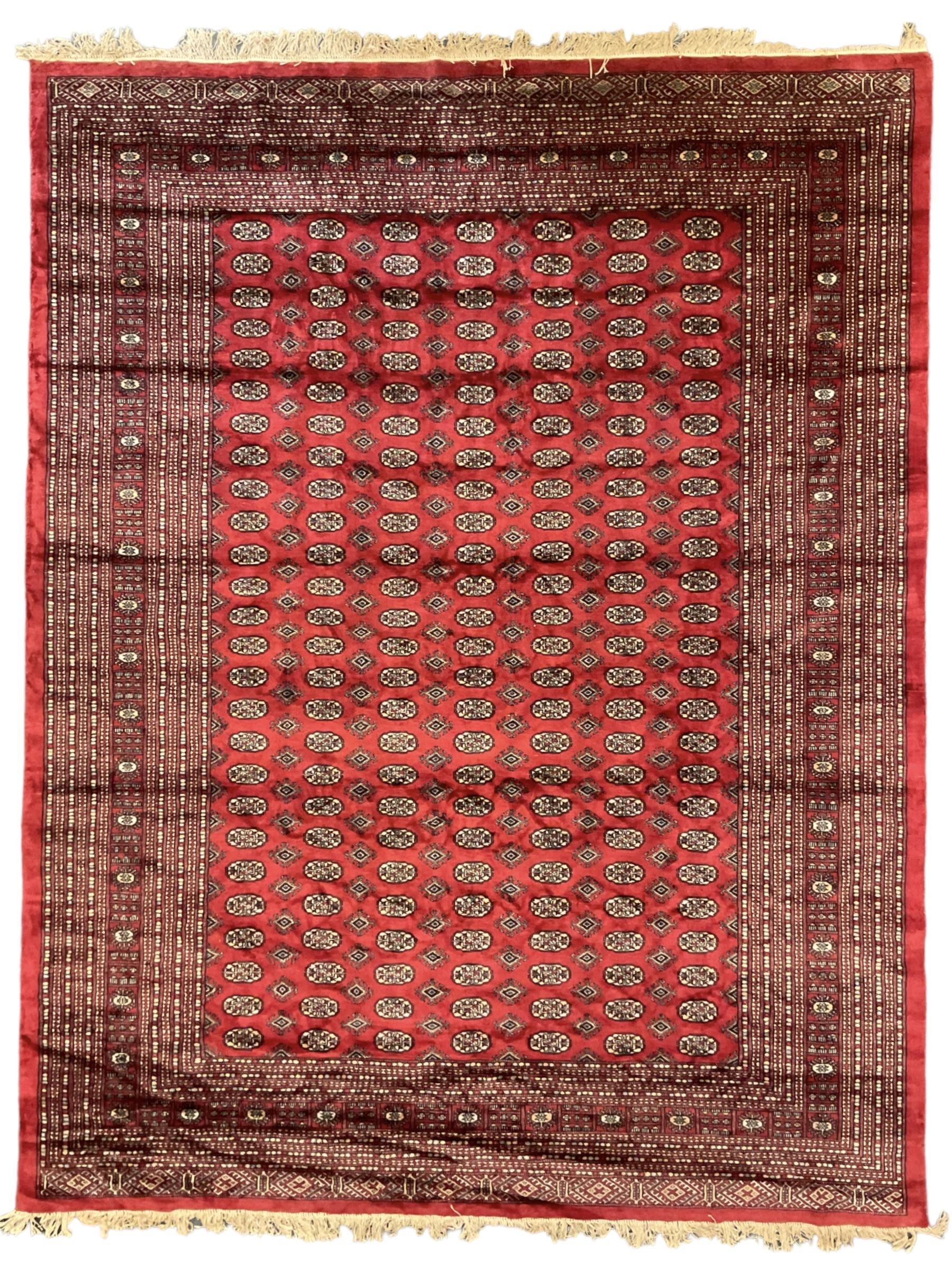 Persian Bokhara crimson ground carpet, the field decorated with repeating Gul motifs and lozenges, the multi-band geometric border with stylised plant motifs, two additional bands at the ends with geometric lozenges