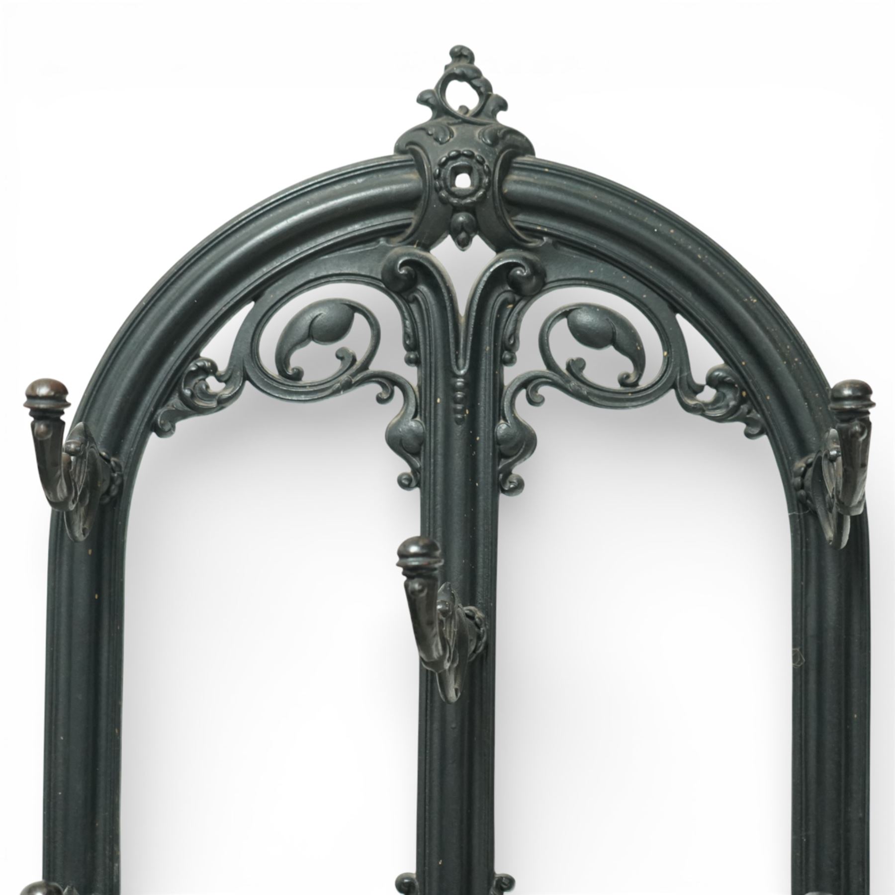 Late 19th century cast iron stick stand, the arched back with scrolling foliate decoration, fitted with multiple hooks, the lower section with pierced panels centred by a radiating sunburst motif, raised on a rectangular drip tray base