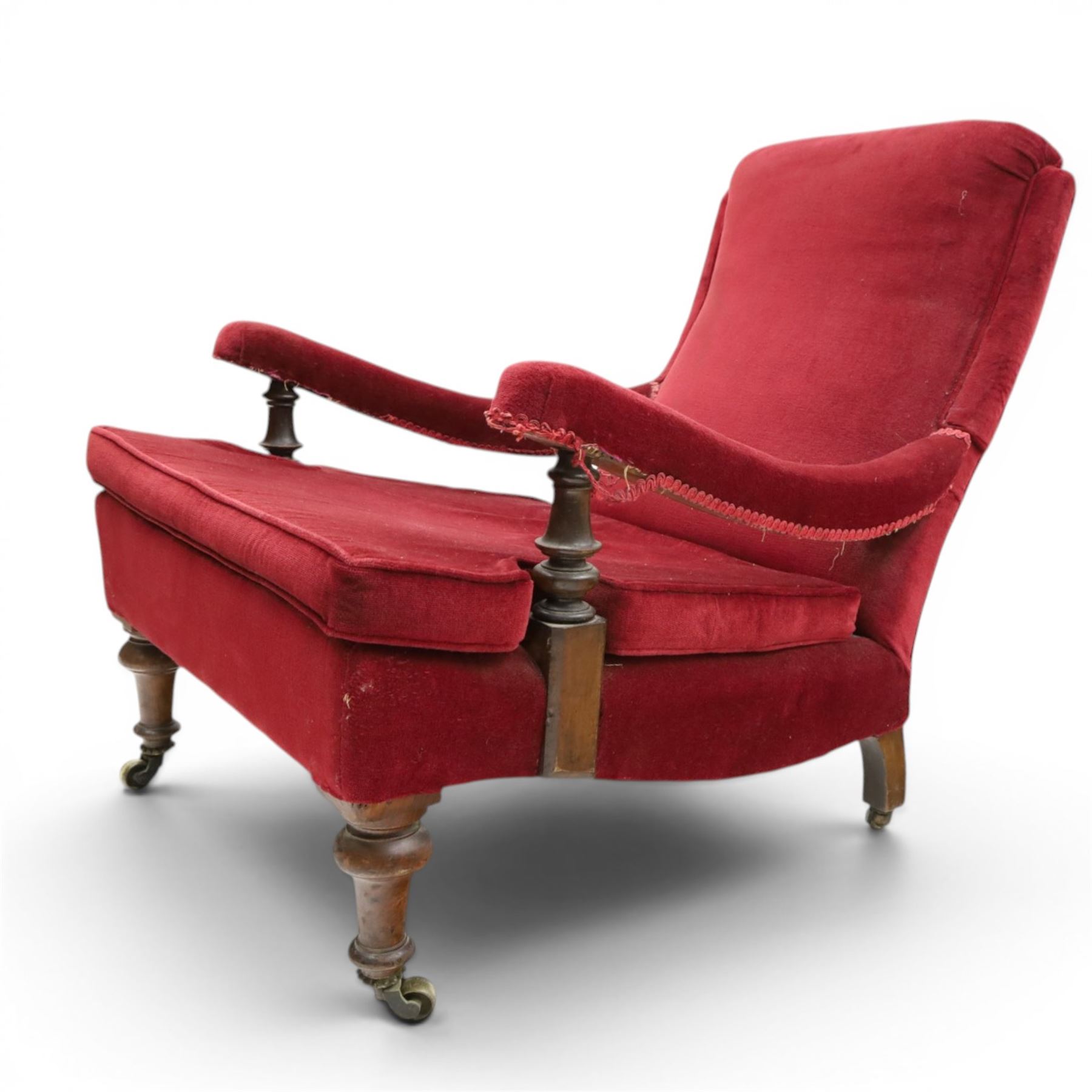 Victorian walnut framed reading open armchair of reclined position, the high sprung back and deep seat upholstered in crimson fabric with matching loose seat cushion, turned arm terminals over turned feet terminating to brass castors