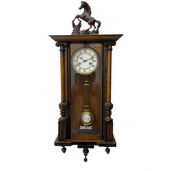 A late 19th century German spring driven 'Vienna' wall clock with a fully glazed door flanked by turned columns with ionic capitals and carving, replacement pediment depicting a prancing horse, with a two-piece enamel dial, Roman numerals, minute track and gothic steel hands, 8-day movement striking the hours and half hours on a gong,  with a gridiron pendulum and beat plate. With key.


