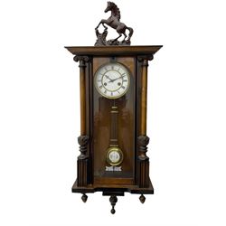A late 19th century German spring driven 'Vienna' wall clock with a fully glazed door flanked by turned columns with ionic capitals and carving, replacement pediment depicting a prancing horse, with a two-piece enamel dial, Roman numerals, minute track and gothic steel hands, 8-day movement striking the hours and half hours on a gong,  with a gridiron pendulum and beat plate. With key.


