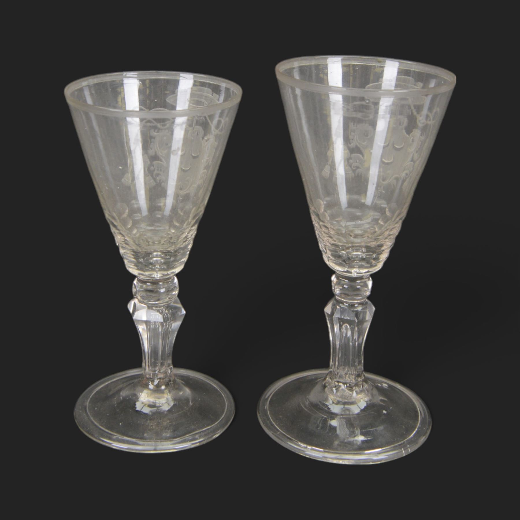 Two 18th century Continental facet cut drinking glasses, each with funnel bowl engraved with armorial type cartouche, upon a knopped and facet cut stem with internal elongated tear, and spreading folded foot, largest H15.5cm