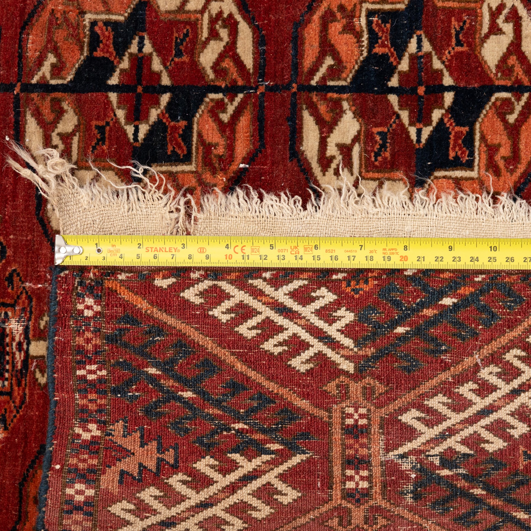 Persian Bokhara crimson ground rug, the field decorated with five rows of repeating Gul motifs with interspersed geometric design, enclosed by a guard band of further geometric-style Gul designs comprised of hook motifs