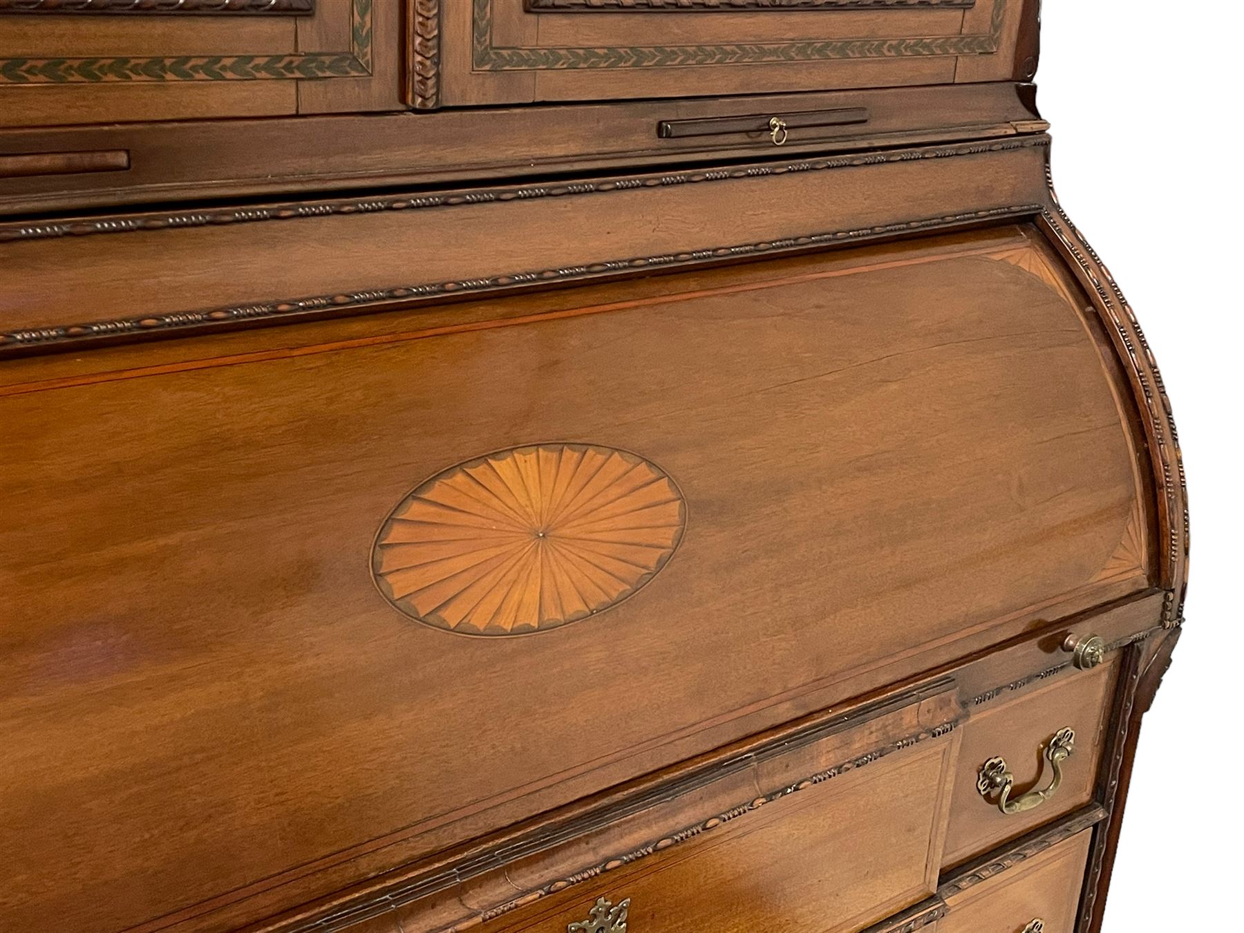 Large and impressive late 19th century Irish mahogany secretaire bookcase, moulded sloped arch dentil pediment decorated with central carved mask surrounded by linen festoons and trailing bellflowers, canted and fluted uprights with carved acanthus leaf upper and lower brackets, enclosed by two astragal glazed doors in the form of trophies with twist ribbon carved mouldings, inlaid with fanned spandrels and trailing leaf painted satinwood band, cylinder roll top inlaid with central fan motif and fanned spandrels, pull-out action revealing stepped fitted interior, central tambour roll cupboard flanked by two Composite pilasters and a combination of drawers and pigeon holes, fitted with three break-front drawers, matched canted and fluted corners with acanthus leaf carvings, on square tapering and fluted spade feet