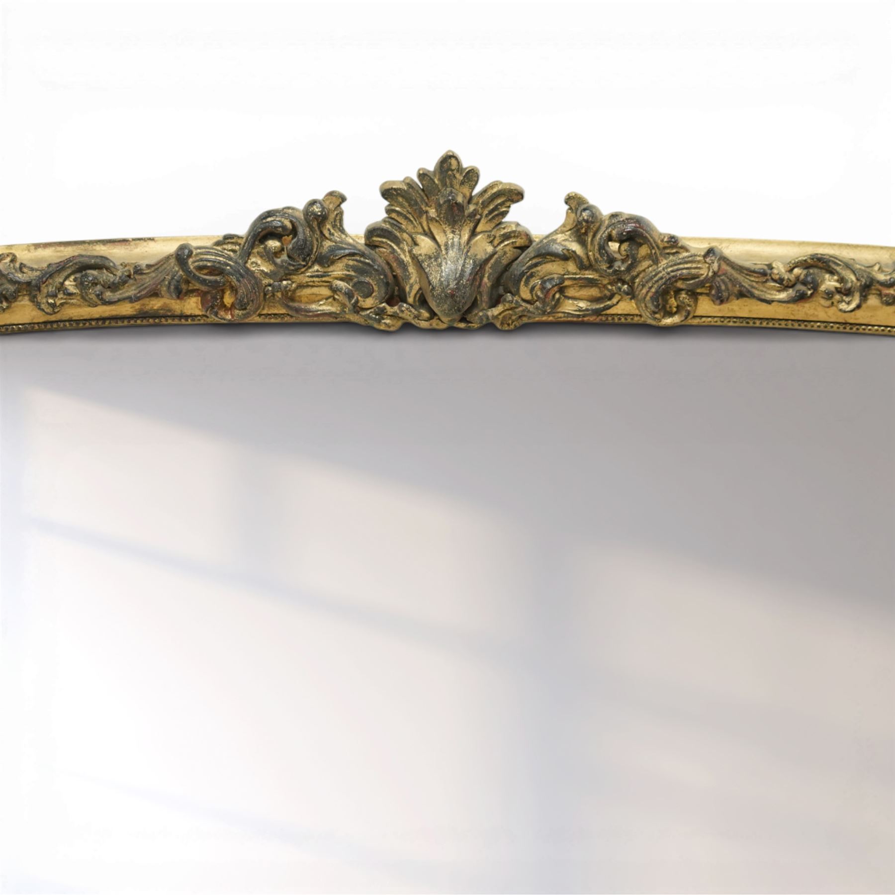 Regency style gilt overmantle mirror, arched rectangular frame with moulded surround, surmounted by a central anthemion and scrolling foliate crest, the frame enriched with beaded and foliate mouldings, the lower corners with applied scroll terminals, enclosing a single rectangular mirror plate