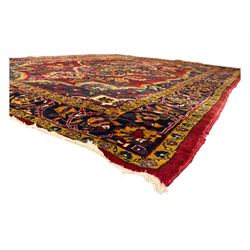 Mid-20th century Persian ground rug, featuring a bold red field and large lobed medallion, flanked by floral corner spandrels, enclosed within multiple borders of stylised vines and palmettes, with fringe to both ends