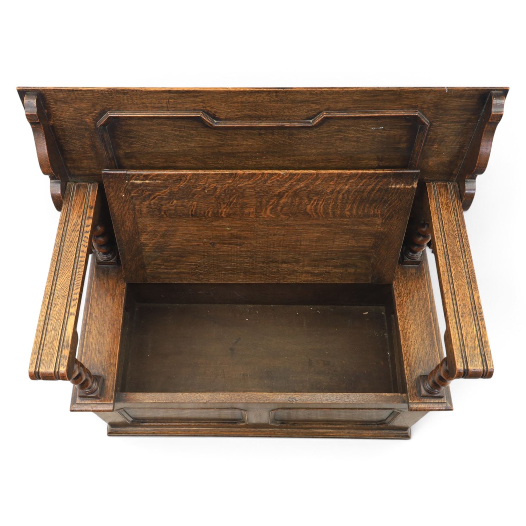Early 20th century oak monks bench, panelled back converting to a table top, reeded armrests with barley twist uprights, hinged seat over panelled base supported on bun feet