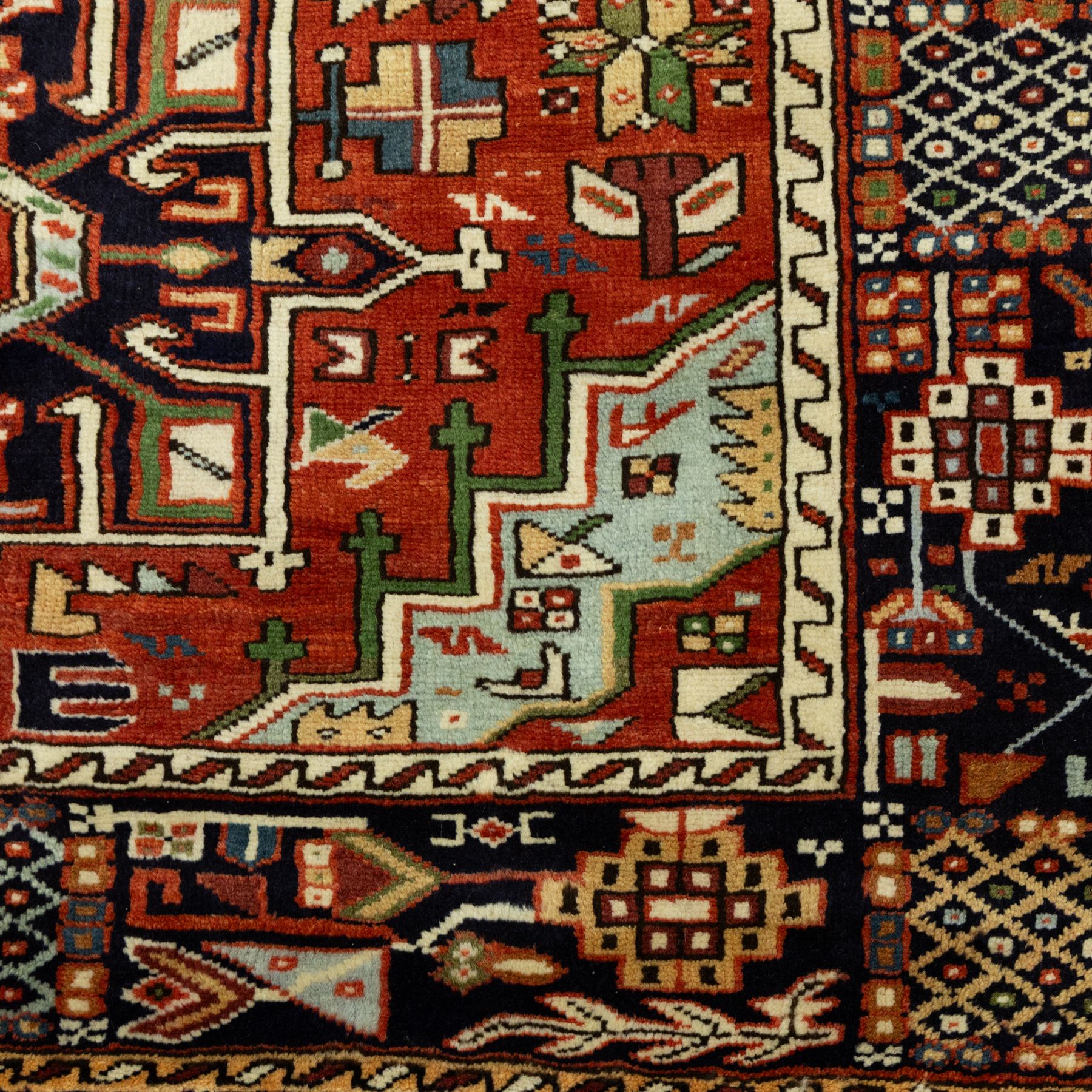 North West Persian Karajeh hand-knotted rug, terracotta ground, with a stepped geometric pole medallion design in blue, ivory and dark navy tones, surrounded by angular tribal motifs incorporating stylised flowerheads, hooked devices and geometric vine work, enclosed by a dark navy border with repeating rosettes and angular leaf motifs, flanked by narrow patterned guard stripes, with cotton fringes