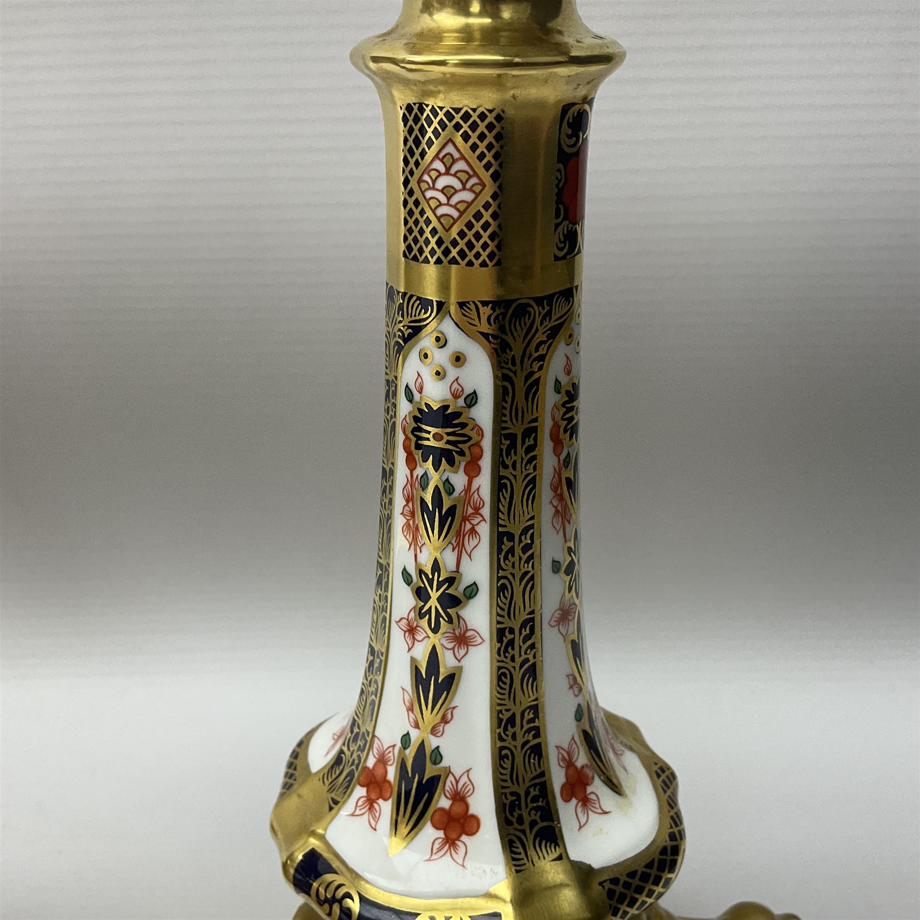 Pair of modern Royal Crown Derby Old Imari 1128 pattern candlesticks, each with shaped drip tray affixed to squat socket, upon spreading stem and canted square base with gilt dolphin edges, with printed marks beneath including Roman numeral year cypher for 2003, H26.5cm, with original boxes
