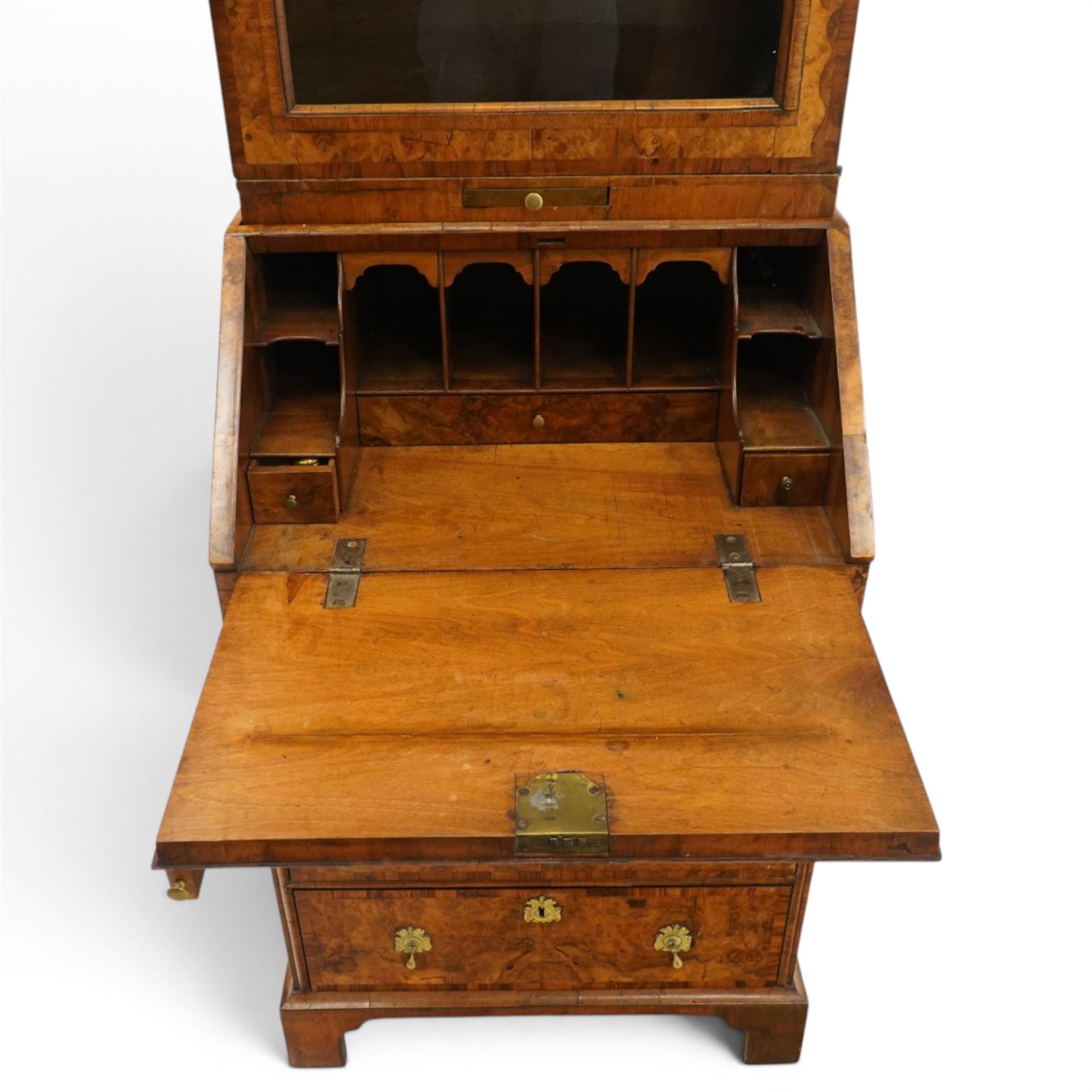 Quality George I figured and burr walnut bureau-cabinet of unusually small proportions, the projecting cavetto cornice over a glazed and banded door enclosing four adjustable shelves, with a candle slide below, the book-matched and banded veneer fall-front enclosing a fitted interior with pigeonholes, correspondence drawers and original trinket boxes and inkwells, over two pull-out stays and four graduating long drawers with banded facias and pressed brass escutcheons and pull handles, lower moulded edge on bracket feet
Provenance: purchased Sotherby's 1977