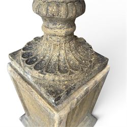 Pair of George III design antiqued composite stone garden urns of campana form, the egg-and-dart everted rim over a waisted body relief moulded with scrolling fruiting foliage and flowerheads, the gadrooned underbelly with twin mask ornaments, the knopped stems on fluted socles, raised on faux panelled square pedestal bases