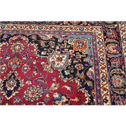 Central Persian Kashan hand-knotted carpet, rose red field, with central shaped lobed medallion issuing an all-over scrolling design of palmettes, floral sprays and arabesques, within conforming spandrels, enclosed by a broad indigo herati type palmette border framed by multiple guard stripes, in a palette of deep red, midnight blue and ivory tones, with cotton fringe ends, and Kashan signature 